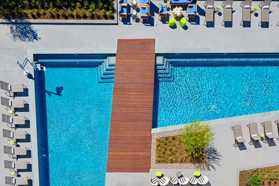 Aerial view of resort pool with wooden deck divider, loungers, and manicured landscaping