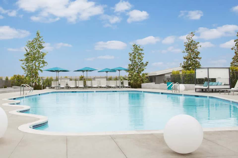 Outdoor resort pool with turquoise umbrellas, loungers, and modern building