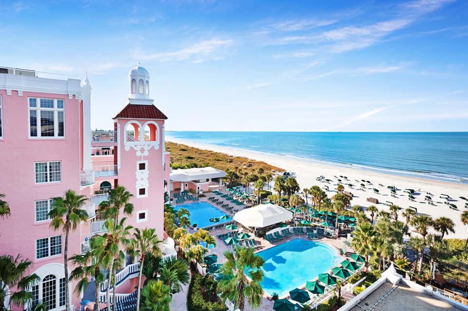 Pink beachfront resort with distinctive tower, multiple pools, palm trees, and sandy beach with ocean view