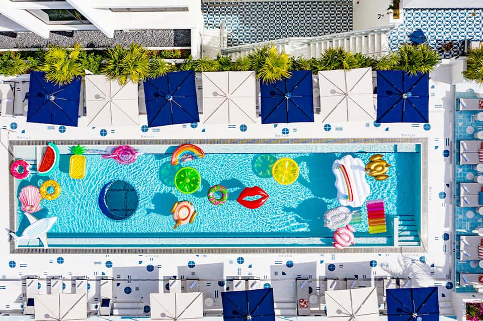 Aerial view of rectangular pool with colorful floats, blue umbrellas, and white lounge chairs