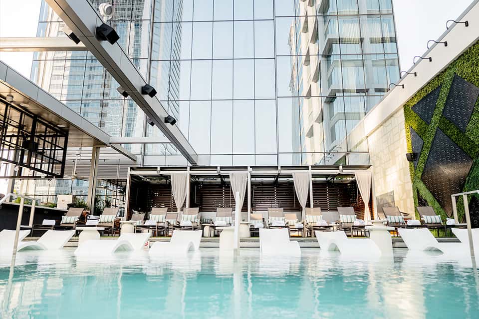 Modern indoor pool with glass ceiling, white loungers, and contemporary hotel architecture