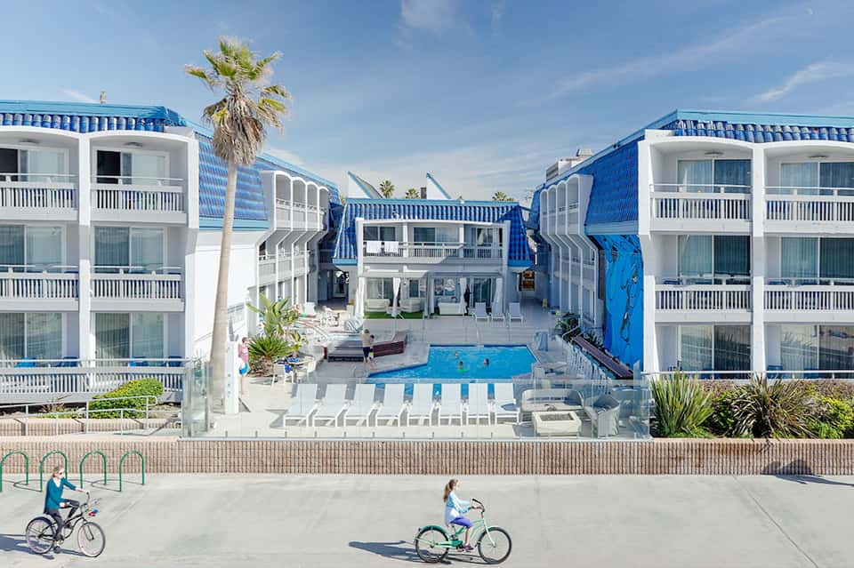Beachfront resort courtyard with blue and white striped umbrellas, pool, and palm trees