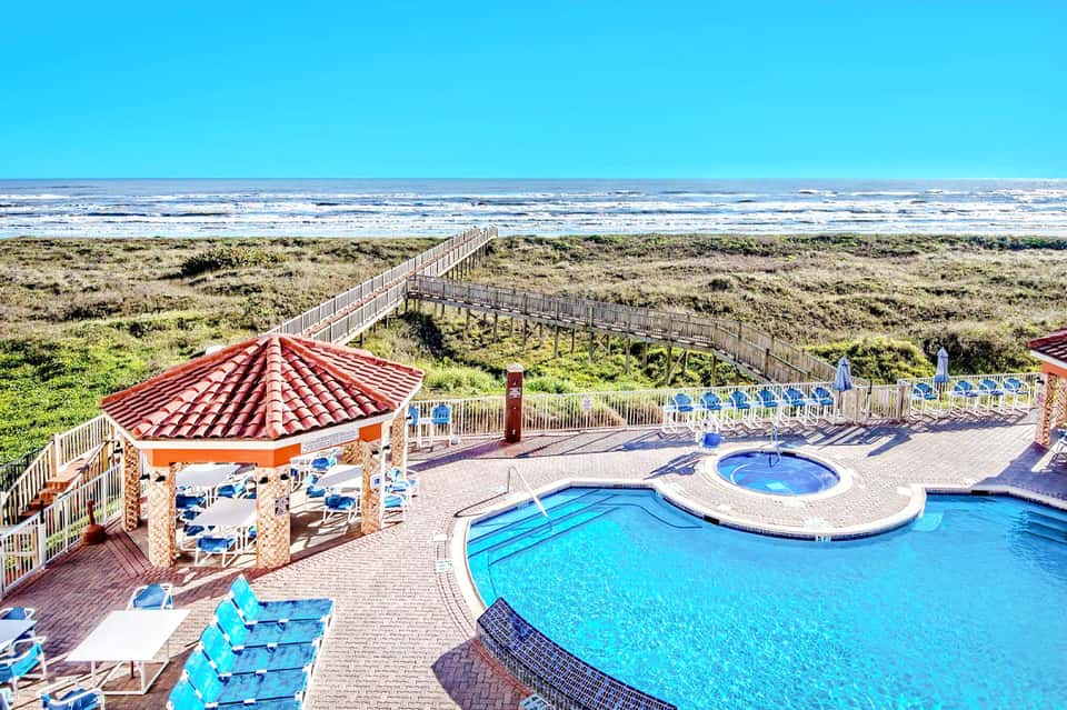 Beachfront resort pool area with cabana, blue loungers, and ocean views on sunny day