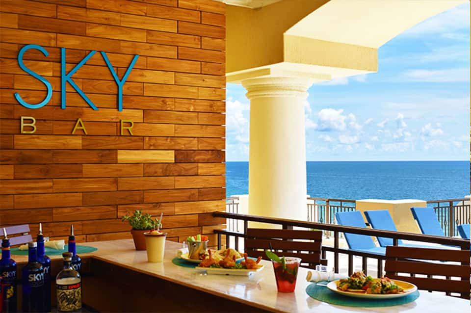 Sky Bar outdoor dining area with ocean views, wooden walls, white columns, and blue SKY BAR signage