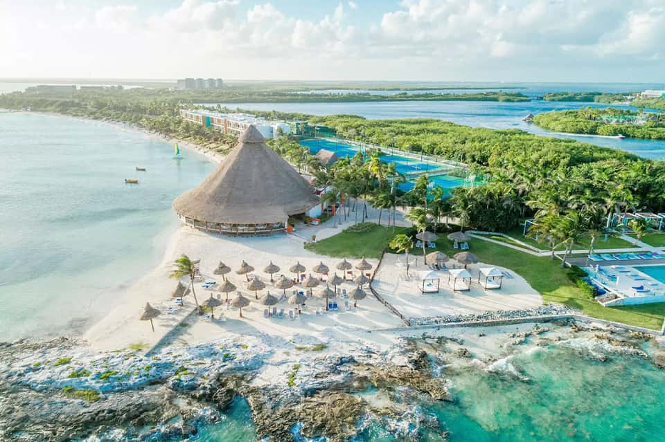 Aerial view of beachfront resort with thatched-roof restaurant, pools, and turquoise Caribbean waters