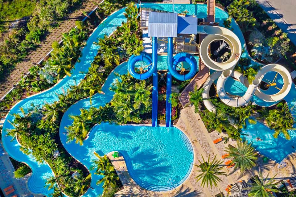 Aerial view of water park with blue slides, lazy river, and tropical landscaping