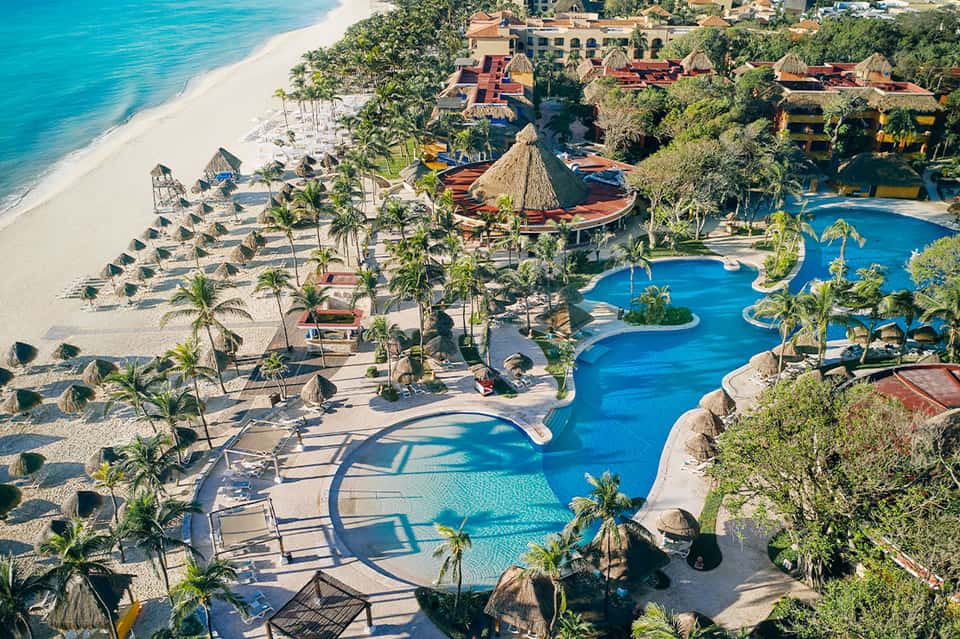 Aerial view of tropical beachfront resort with multiple pools, palm trees, and beach