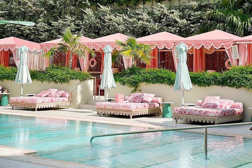 Resort pool area with pink cabanas, umbrellas, and lounge seating under decorative tents