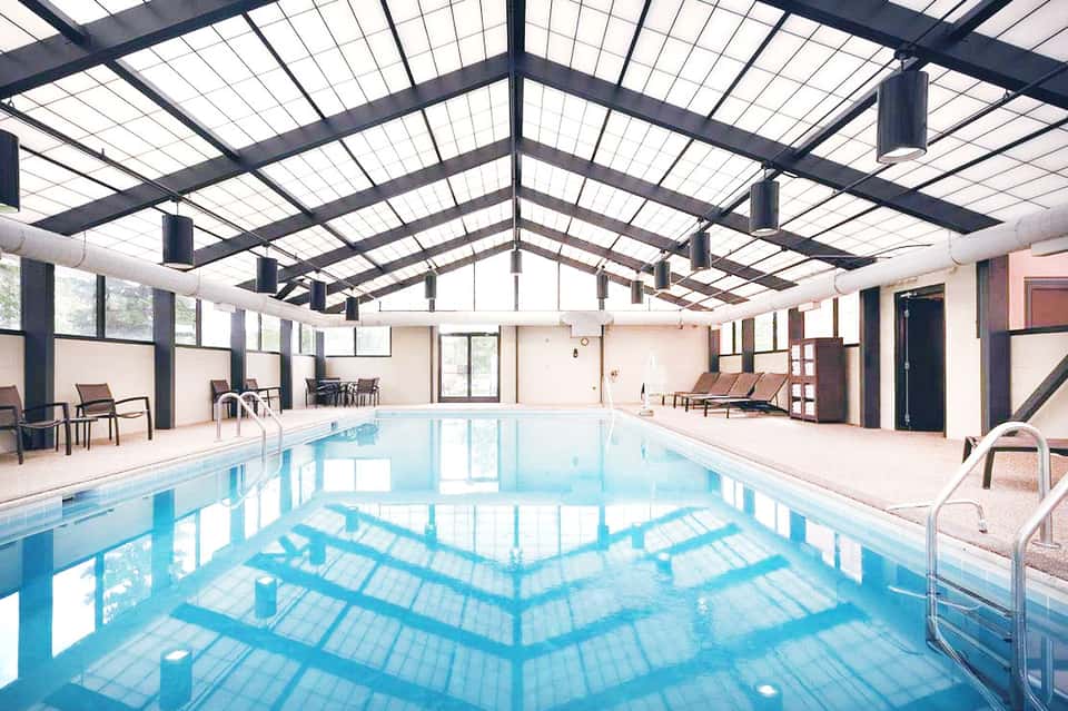 Indoor lap pool with skylighting, lounge chairs, and accessible deck space in modern facility