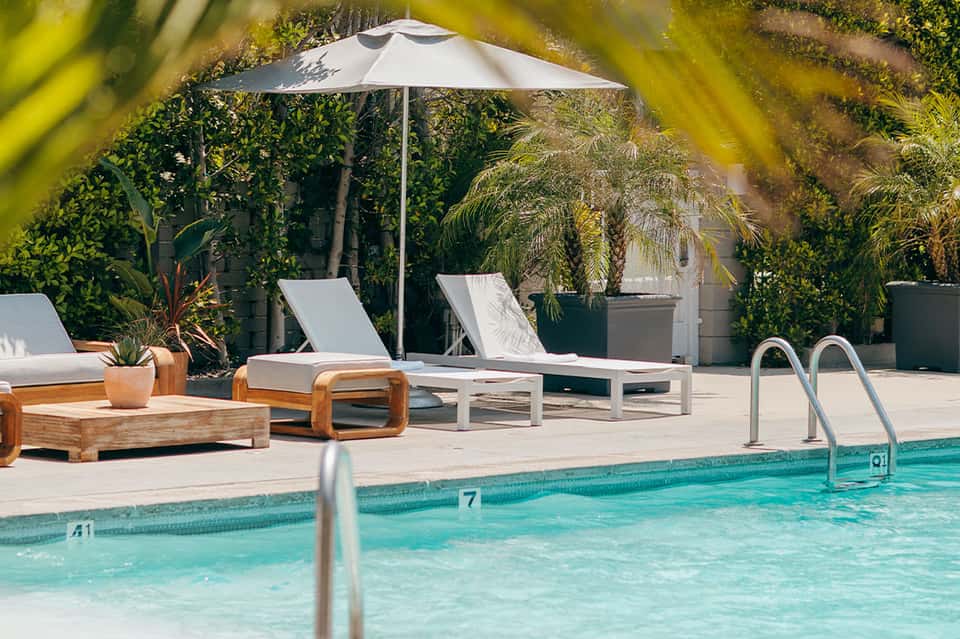 Pool area with white lounge chairs, umbrella, lush greenery, and turquoise water