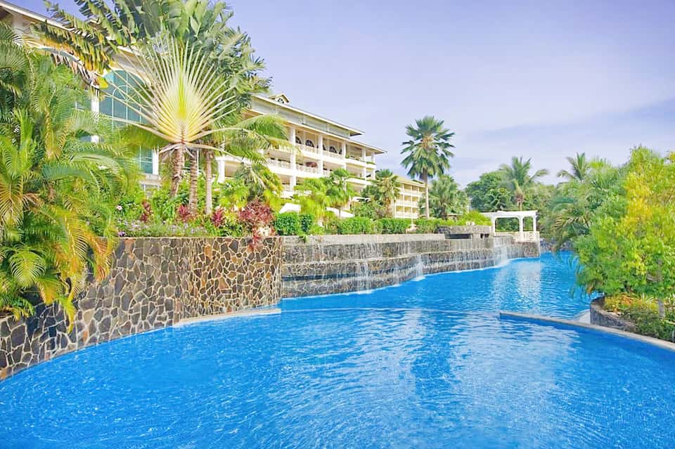 Resort infinity pool surrounded by tropical landscaping and modern building architecture