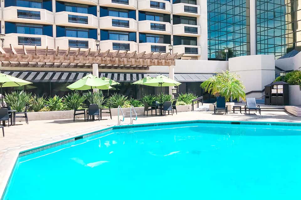 Resort pool with bright turquoise water, lounge chairs, lime umbrellas, and high-rise hotel
