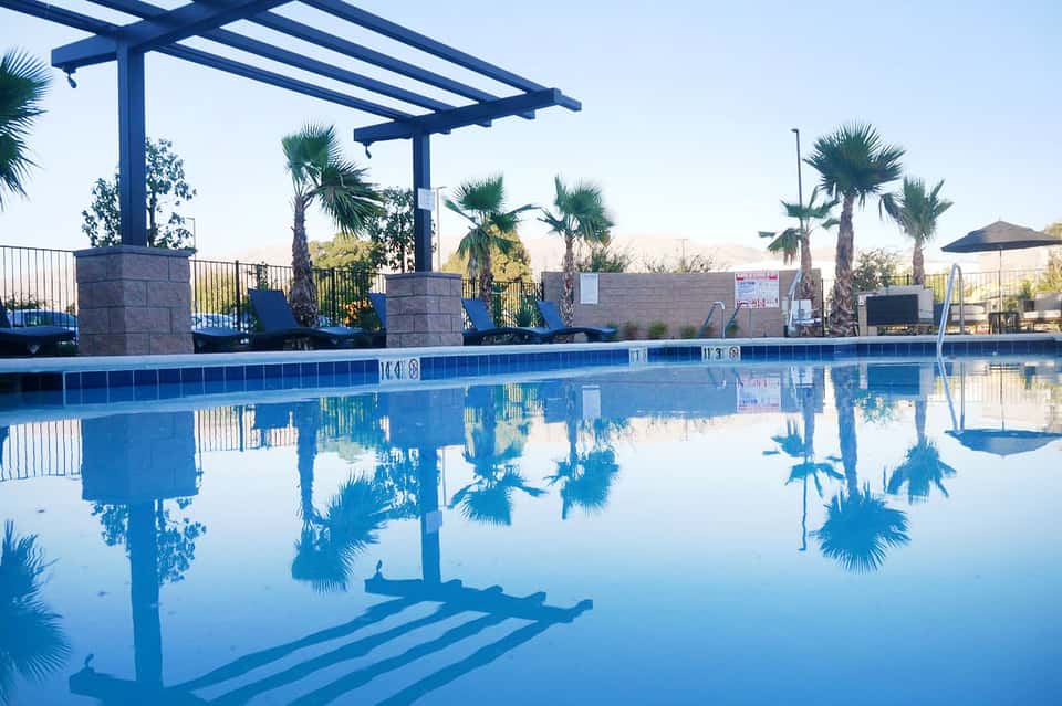 Resort pool with pergola structure, palm trees, and clear blue water at dusk