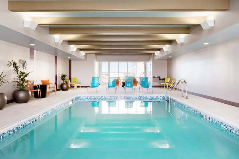 Indoor lap pool with skylights, colorful lounge chairs, and modern ceiling beams