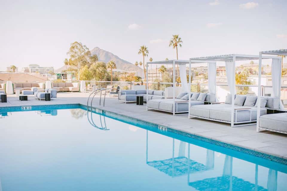 Outdoor rooftop pool with modern white cabanas and mountain city views at sunset