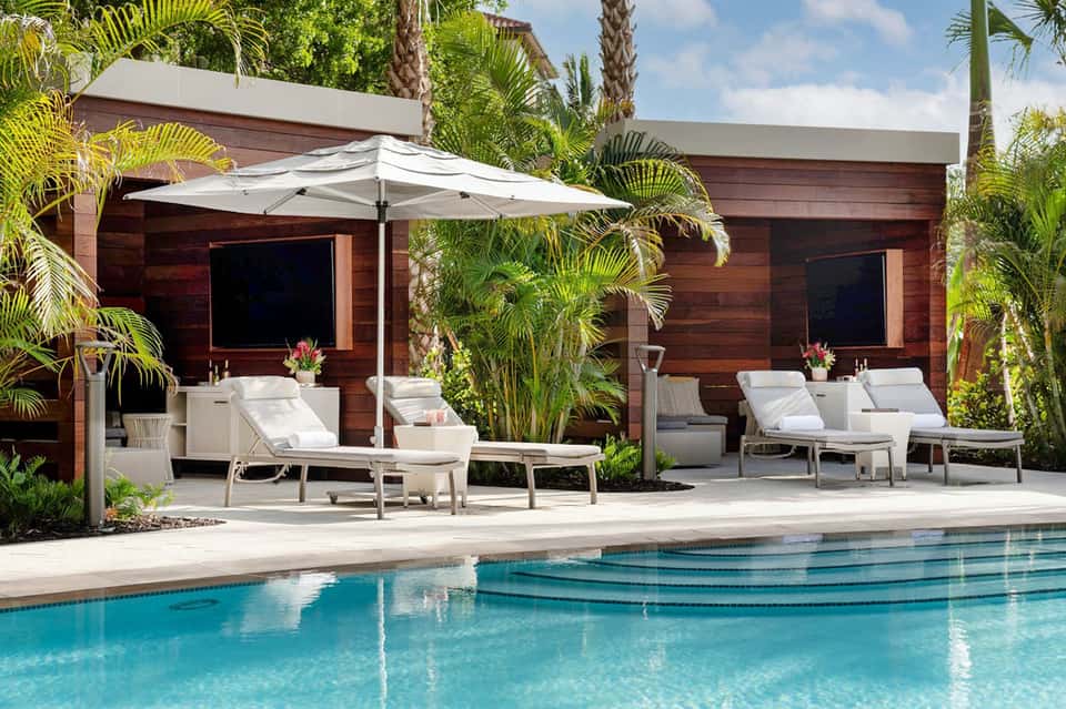 Modern poolside cabanas with white umbrellas, loungers, and palm trees beside turquoise pool