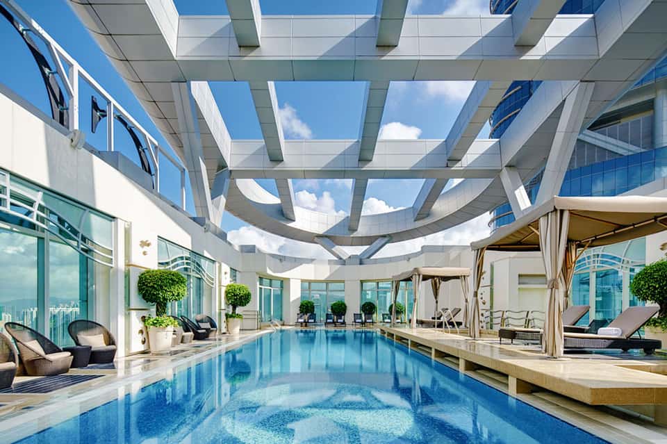 Luxury indoor pool with glass ceiling, lounge chairs, and city skyline views