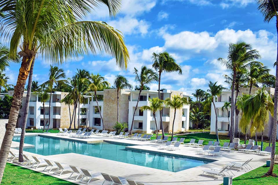 Modern resort with white building, pool lined with loungers, and surrounding palm trees