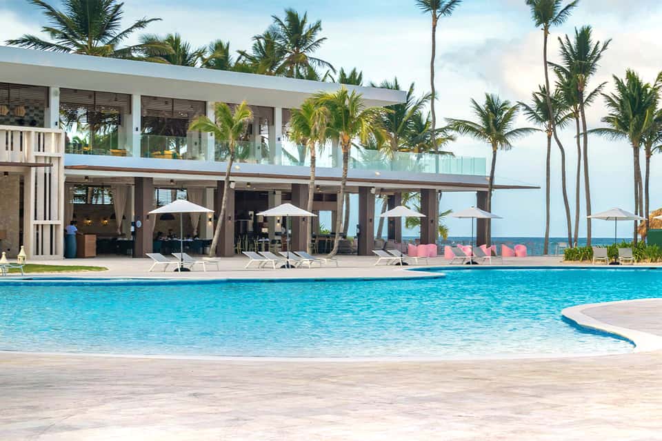 Beachfront resort pool with modern pavilion, palm trees, and ocean views