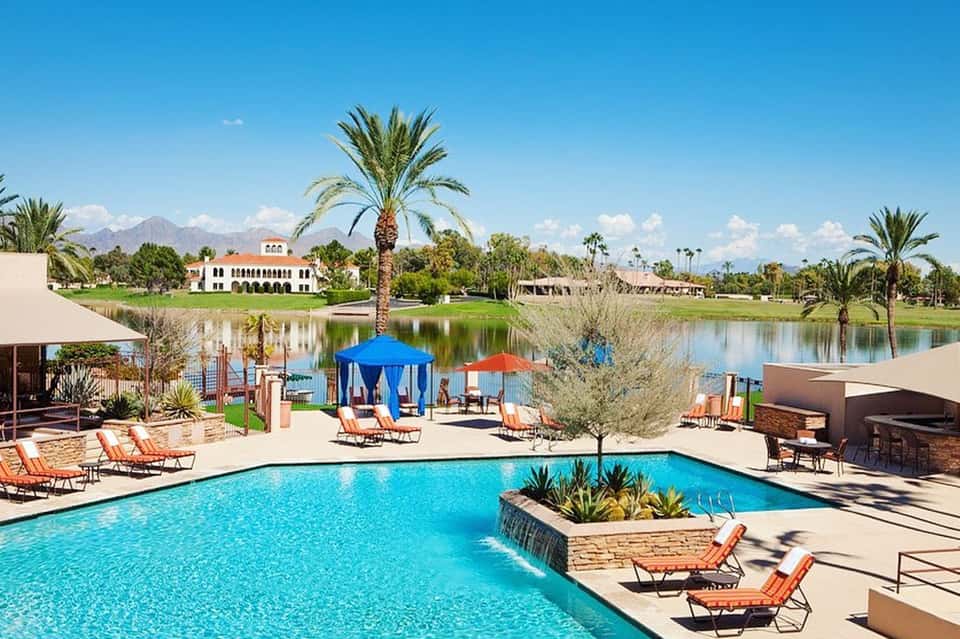 Resort pool with blue water, lounge chairs, and palm trees with mountains in background
