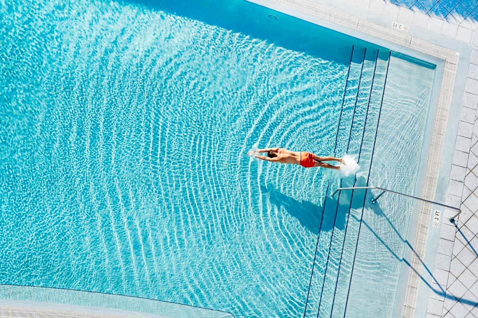 Aerial view of swimmer doing laps in crystal-clear rectangular pool with lane markings