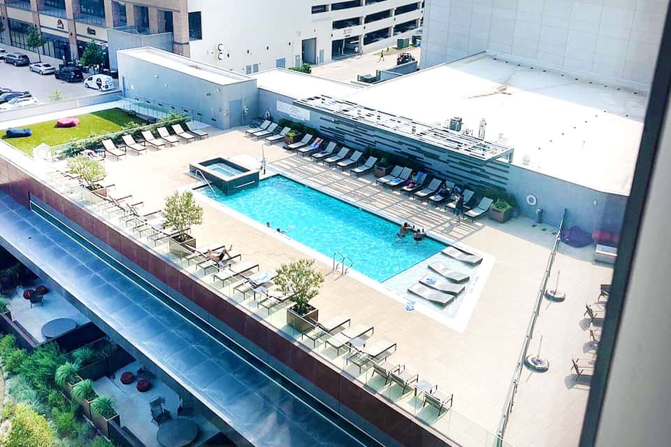 Aerial view of resort pool deck with lounge chairs, hot tub, and surrounding buildings
