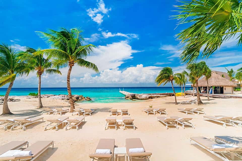 Pristine tropical beach with lounge chairs, palm trees, thatched roof hut, and crystal waters