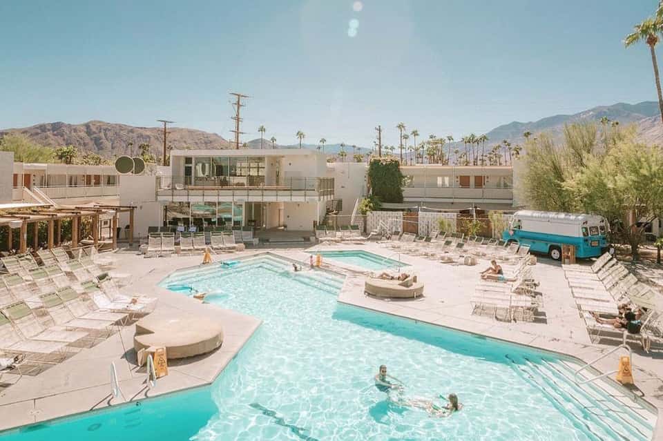 Desert resort with multiple turquoise pools, mid-century modern architecture, palm trees, and mountains