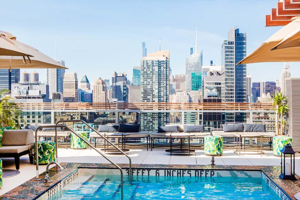 Rooftop pool with Chicago skyline view, lounge seating, tan umbrellas, and modern high-rise buildings
