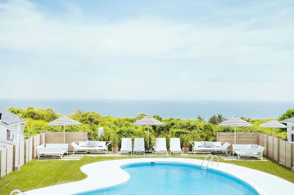 Curved pool surrounded by green lawn, striped umbrellas, and ocean horizon view