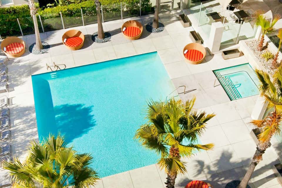 Aerial view of bright turquoise resort pool with orange circular loungers and palm trees