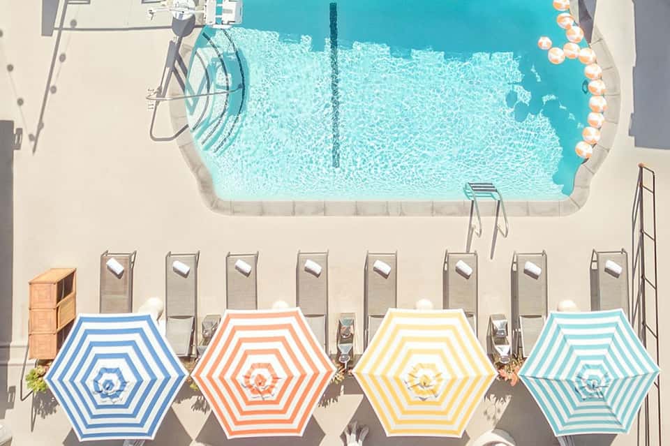 Aerial view of resort pool with colorful striped umbrellas and lounge chairs on white deck