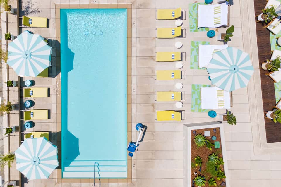 Aerial view of resort pool with yellow loungers, striped umbrellas, and surrounding patios