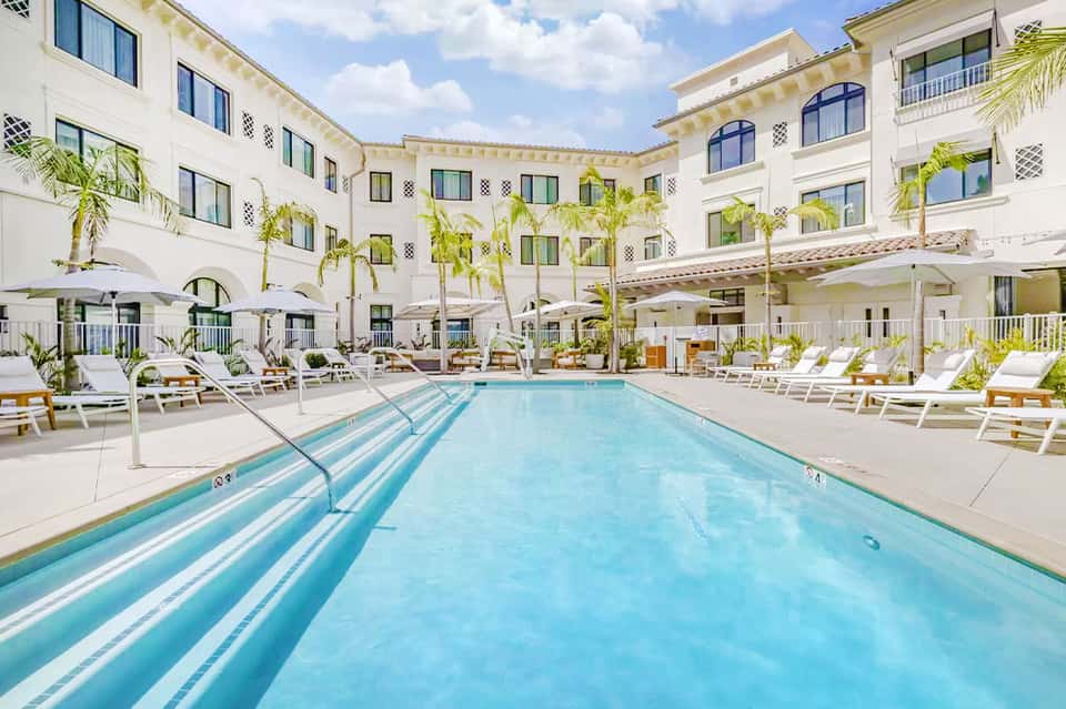 Resort swimming pool with lane markers surrounded by white loungers and palm trees