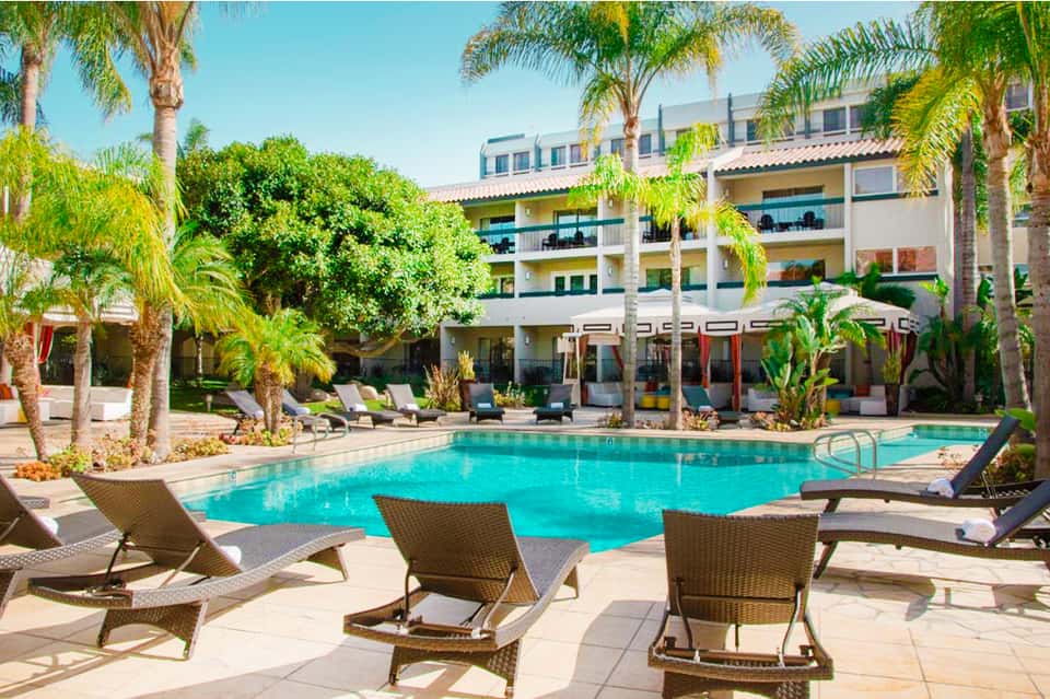 Resort courtyard pool with palm trees, loungers, and multi-story hotel buildings