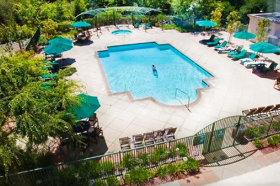 Resort pool surrounded by turquoise umbrellas, lounge chairs, and lush green landscaping