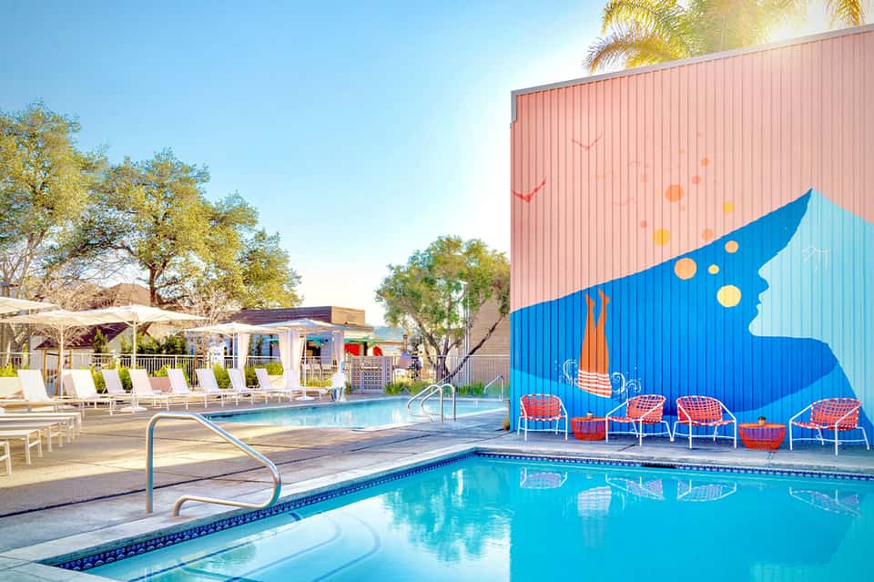 Resort pool area with colorful mural wall, red loungers, and palm trees under blue sky