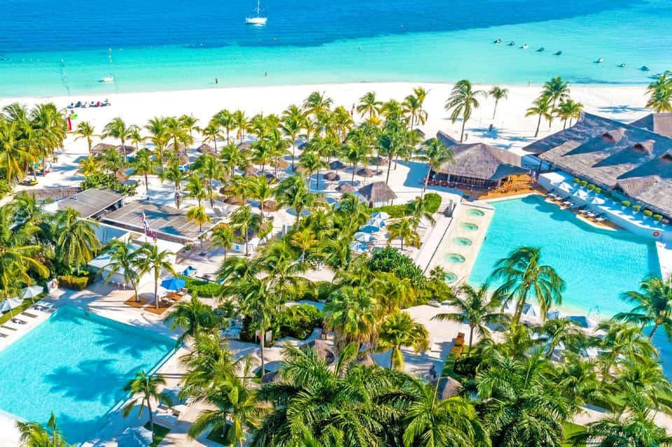 Aerial view of beachfront resort with multiple pools, white sand beach, and palm trees
