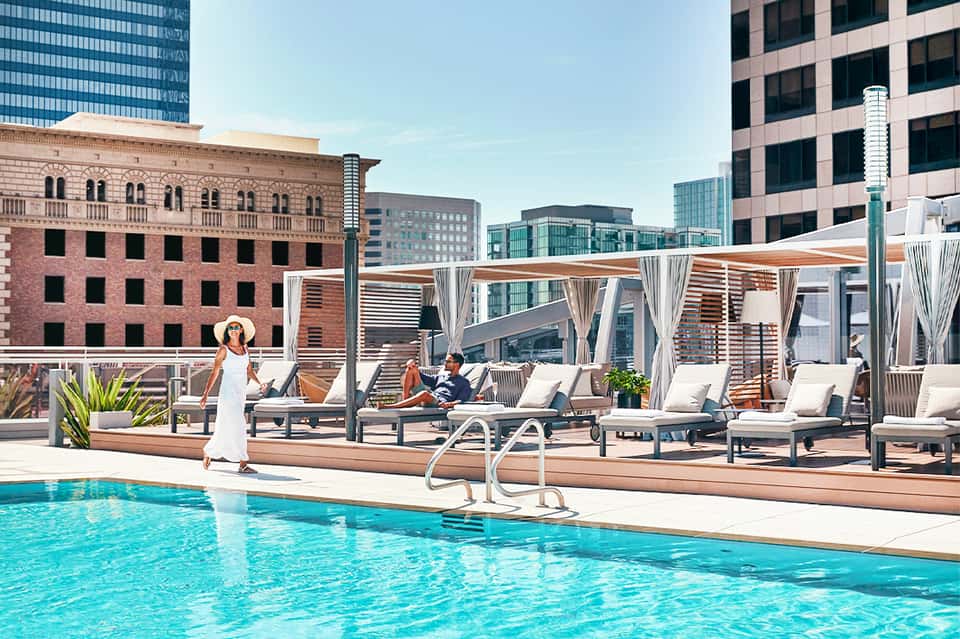 Rooftop pool at urban hotel with city skyline, lounge chairs, and white cabanas with curtains