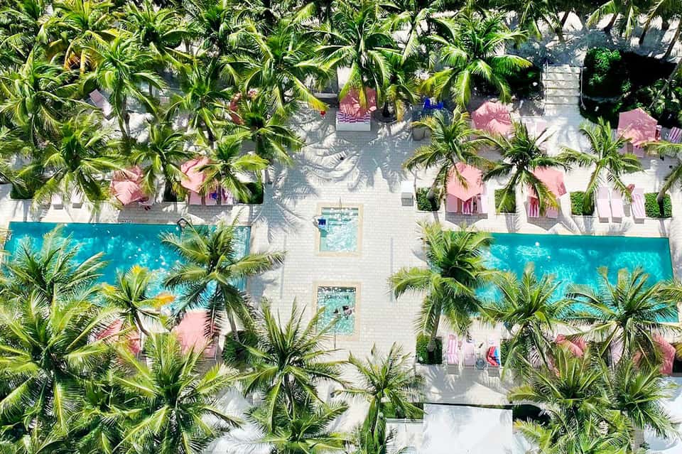 Aerial view of modern resort courtyard with turquoise pools, palm trees, and pink-roofed buildings