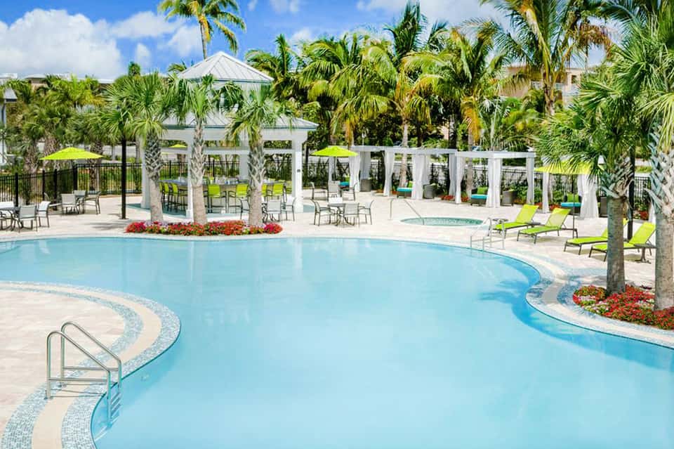 Resort pool with curved shape, white pergolas, palm trees, and lounge chairs