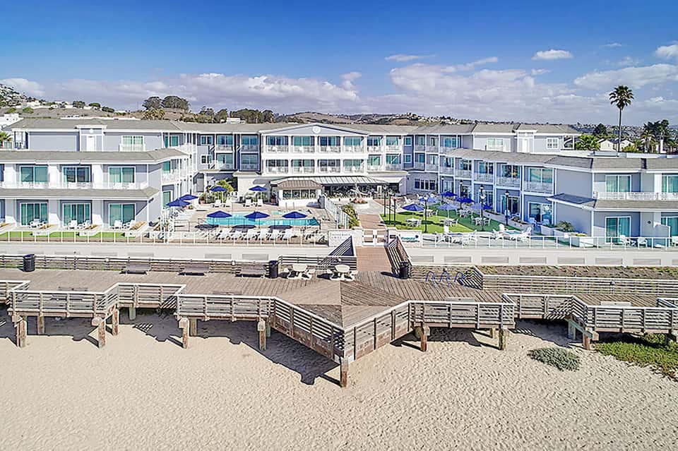 Modern beachfront resort with white architecture, blue umbrellas, and manicured grounds