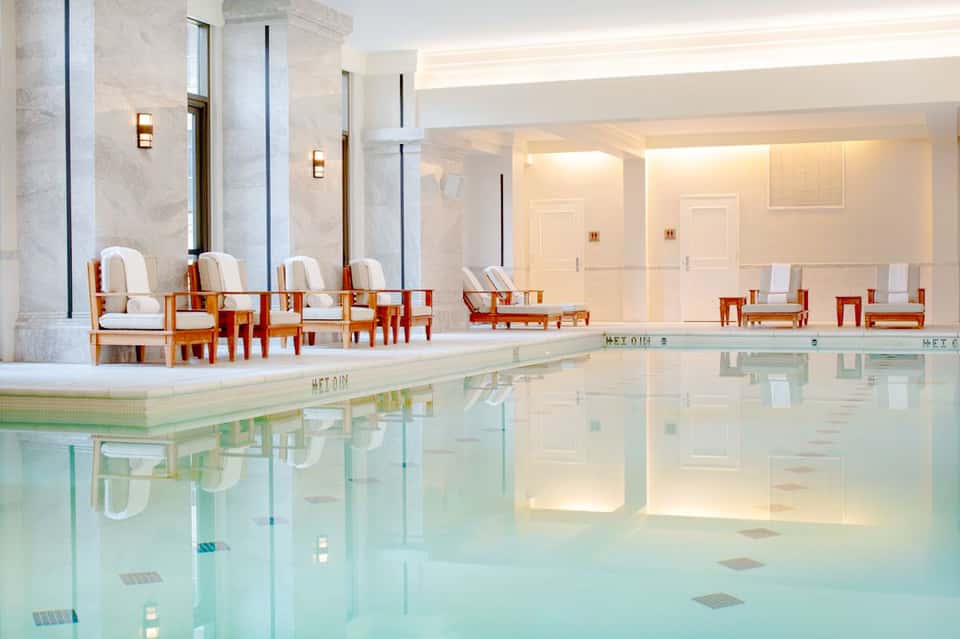 Luxurious indoor pool with marble columns, elegant cream seating, and soft ambient lighting