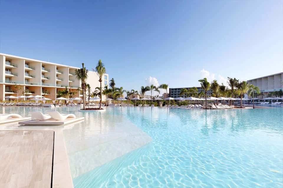 Modern resort pool with white loungers, palm trees, and contemporary hotel architecture
