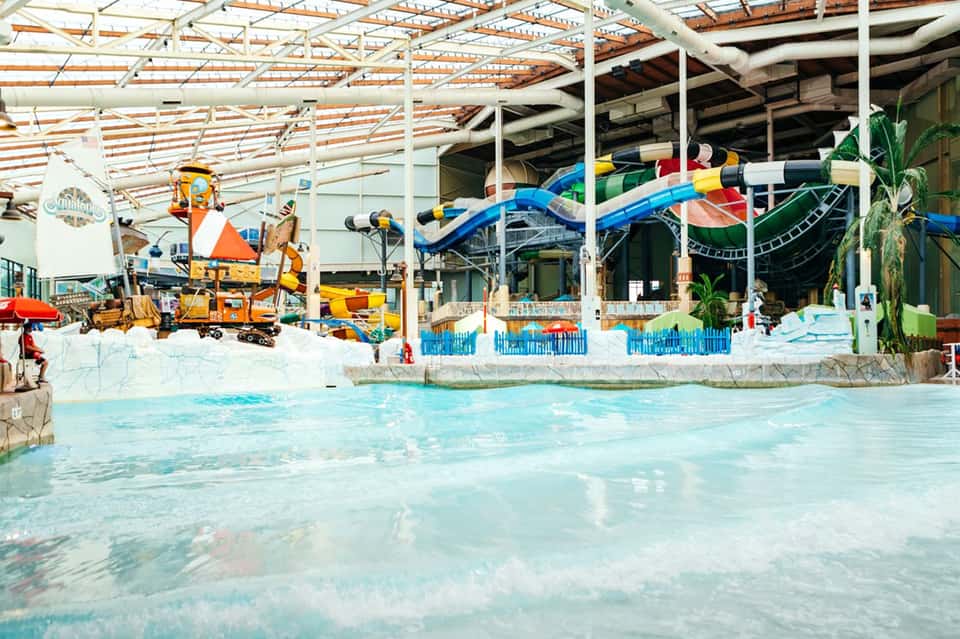 Indoor water park with retractable roof, colorful waterslides, shallow pools, and tropical themed entertainment area