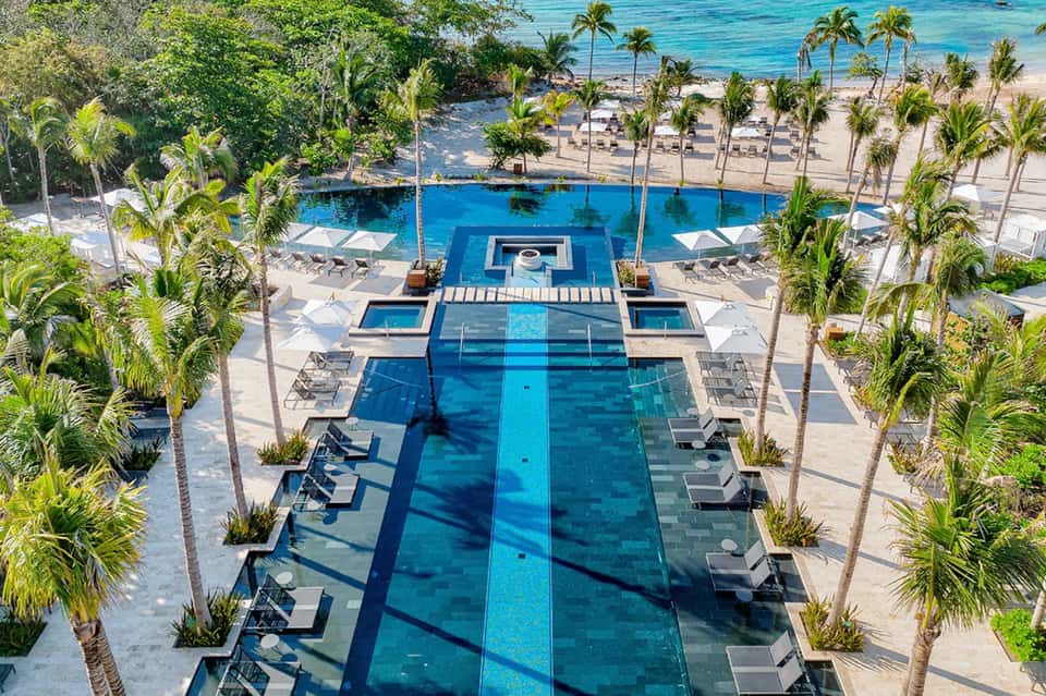 Aerial view of resort lap pools with palm trees, beach access, and lounge seating