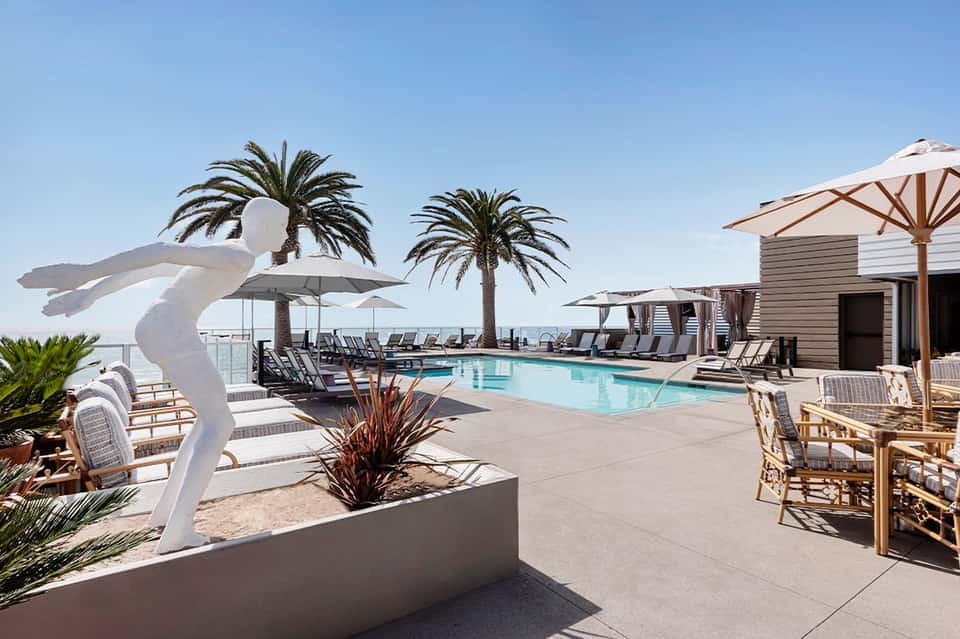 Upscale beachfront pool area with palm trees, loungers, white sculpture, and ocean views