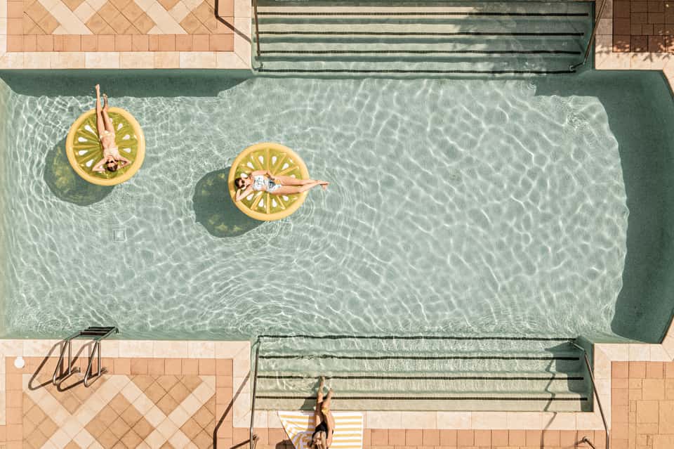 Aerial view of swimming pool with two people on yellow floats in clear turquoise water