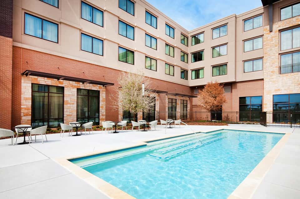 Indoor courtyard pool at brick hotel with lounge chairs, modern windows, and landscaping