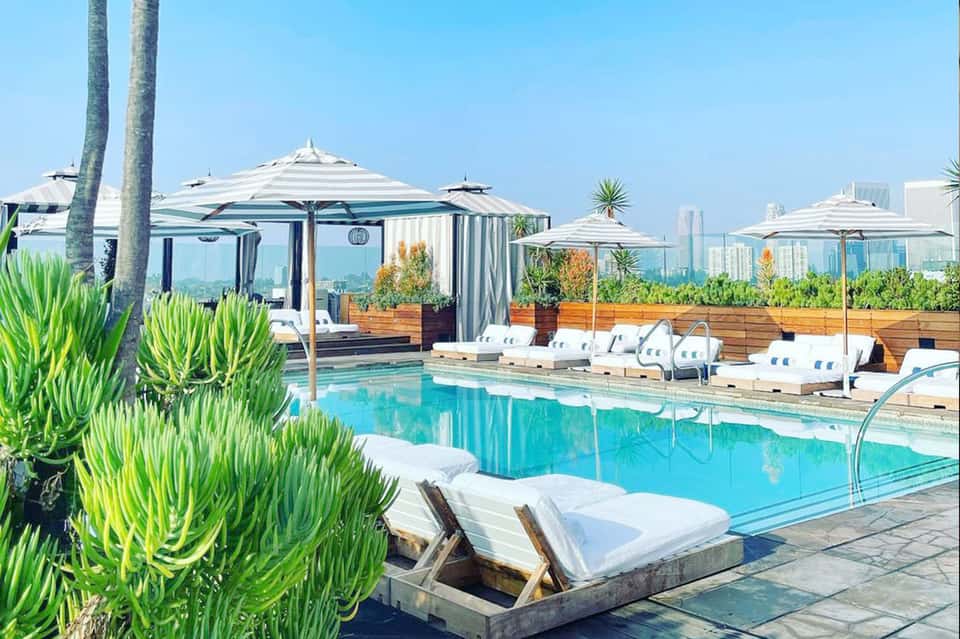 Rooftop pool with turquoise water, white lounge chairs, umbrellas, and city skyline views in background